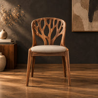 Wooden chair with a carved branch pattern back and a pale fabric seat in a dark studio against a charcoal plaster wall