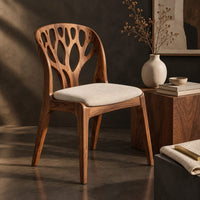 Corner detail of wooden chair with a carved branch pattern back and a pale fabric seat beside wood, brass and linen samples