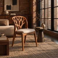 Wooden chair with a carved branch pattern back and a pale fabric seat in an industrial loft living room with exposed brick