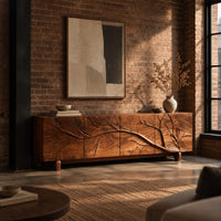 Tv stand with a carved branch relief across four front panels in an industrial loft living room with exposed brick