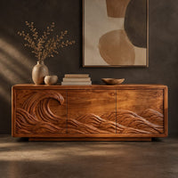 Corner detail of sideboard with a breaking wave carved across three doors beside wood, brass and linen samples