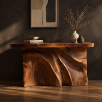 Console table with a thick slab top over a carved body of flowing ridges, three-quarter view showing the grain
