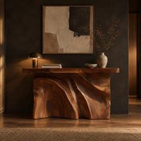 Console table with a thick slab top over a carved body of flowing ridges in a dark entryway at golden hour