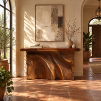 Console table with a thick slab top over a carved body of flowing ridges in a bright entryway with arched windows and plants