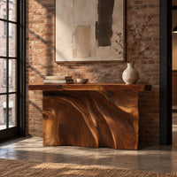 Console table with a thick slab top over a carved body of flowing ridges in an industrial loft entryway with exposed brick