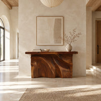 Console table with a thick slab top over a carved body of flowing ridges in a bright open plan entryway