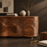 Corner detail of sideboard with carved contour waves and curved ends on block feet beside wood, brass and linen samples