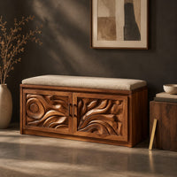 Corner detail of shoe bench with two carved relief doors and a padded seat on top beside wood, brass and linen samples