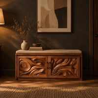 Shoe bench with two carved relief doors and a padded seat on top in a dark entryway at golden hour