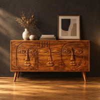 Mid century sideboard with three carved faces and four tapered legs in a dark studio against a charcoal plaster wall