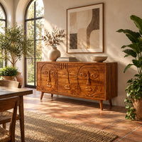 Mid century sideboard with three carved faces and four tapered legs in a bright dining room with arched windows and plants