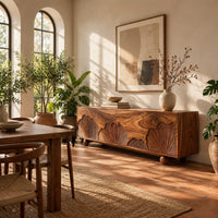 Sideboard with carved fan motifs across four panels and ball feet in a bright dining room with arched windows and plants