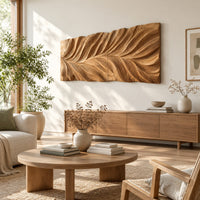 Wide wall art panel carved in a feather shaped leaf with sweeping ridges in a bright sunroom with green plants