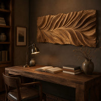 Wide wall art panel carved in a feather shaped leaf with sweeping ridges above a desk in a dark study corner