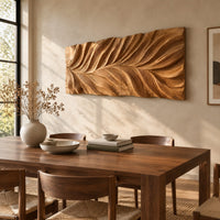 Wide wall art panel carved in a feather shaped leaf with sweeping ridges beside a dining table in natural light