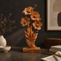 Corner detail of carved wood flower sculpture with open blossoms and leaves on a block base beside wood, brass and linen samples