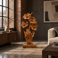 Carved wood flower sculpture with open blossoms and leaves on a block base in an industrial loft living room with exposed brick