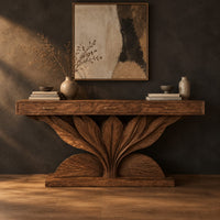 Console table with a carved leaf fan base and three drawer fronts in a dark studio against a charcoal plaster wall