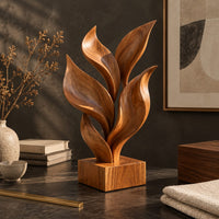 Corner detail of sculpture of smooth carved leaves rising from a square block base beside wood, brass and linen samples