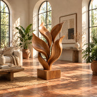 Sculpture of smooth carved leaves rising from a square block base in a bright living room with arched windows and plants