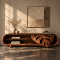 Corner detail of capsule shaped tv stand with open shelves and a carved leaf panel beside wood, brass and linen samples