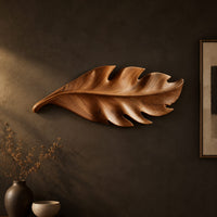 Leaf shaped wall art in wood with notched lobes and carved veins on a dark charcoal plaster wall