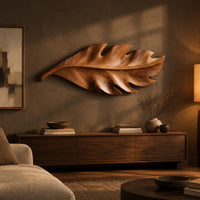 Leaf shaped wall art in wood with notched lobes and carved veins above a low console in an evening living room