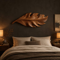 Leaf shaped wall art in wood with notched lobes and carved veins above a bed in a dusk lit bedroom