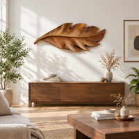 Leaf shaped wall art in wood with notched lobes and carved veins in a bright sunroom with green plants