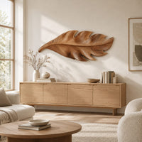 Leaf shaped wall art in wood with notched lobes and carved veins above a light oak sideboard in daylight