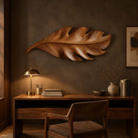 Leaf shaped wall art in wood with notched lobes and carved veins above a desk in a dark study corner