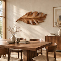 Leaf shaped wall art in wood with notched lobes and carved veins beside a dining table in natural light