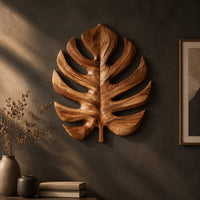 Monstera leaf carved from wood with deep slits and a short stem on a dark charcoal plaster wall
