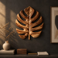 Detail of monstera leaf carved from wood with deep slits and a short stem beside wood, brass and linen samples