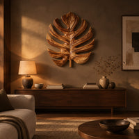 Monstera leaf carved from wood with deep slits and a short stem above a low console in an evening living room