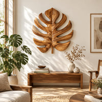 Monstera leaf carved from wood with deep slits and a short stem in a bright sunroom with green plants