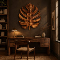 Monstera leaf carved from wood with deep slits and a short stem above a desk in a dark study corner