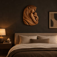 Wall art carved as a mother holding her child, with long flowing hair above a bed in a dusk lit bedroom