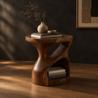 Carved pedestal side table with a twisting opening and a low open nook, three-quarter view showing the grain