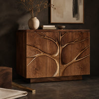 Corner detail of two door sideboard with a carved tree branch relief across the fronts beside wood, brass and linen samples