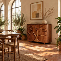 Two door sideboard with a carved tree branch relief in a bright dining room with arched windows and plants