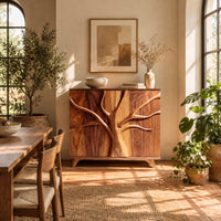 Two door sideboard with a carved tree branch relief across the doors in a bright dining room with arched windows and plants