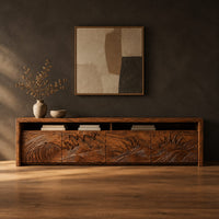 Long tv stand with four carved doors showing ocean waves and a rising sun in a dark studio against a charcoal plaster wall