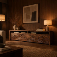 Long tv stand with four carved doors showing ocean waves and a rising sun in an evening living room with walnut wall paneling