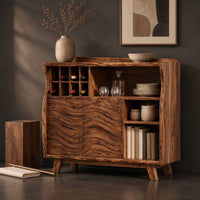 Corner detail of bar cabinet with carved wave doors, a wine slot grid and open shelves beside wood, brass and linen samples