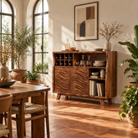 Bar cabinet with carved wave doors, a wine slot grid and open shelves in a bright dining room with arched windows and plants