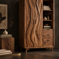 Corner detail of wardrobe with carved wave pattern doors beside open shelves and three drawers beside wood, brass and linen samples