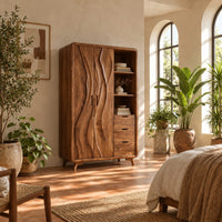 Wardrobe with carved wave pattern doors beside open shelves and three drawers in a bright bedroom with arched windows and plants
