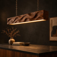 Long wood pendant light with carved waves and a warm glow along its underside, three-quarter view showing the grain