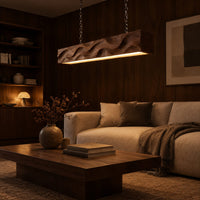 Long wood pendant light with carved waves and a warm glow along its underside in an evening living room with walnut wall paneling